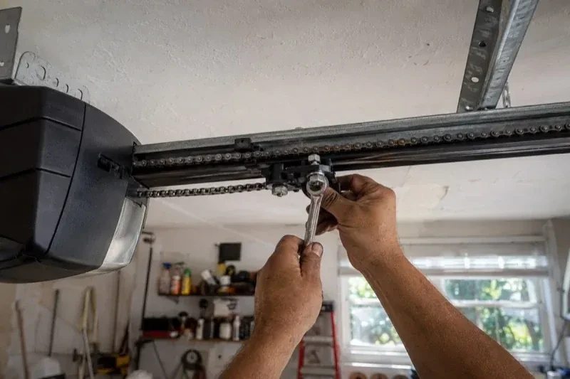 Hands holding a wrench against an opener trolley beneath a chain rail — Chain-Drive Opener Repair, Kawartha Lakes