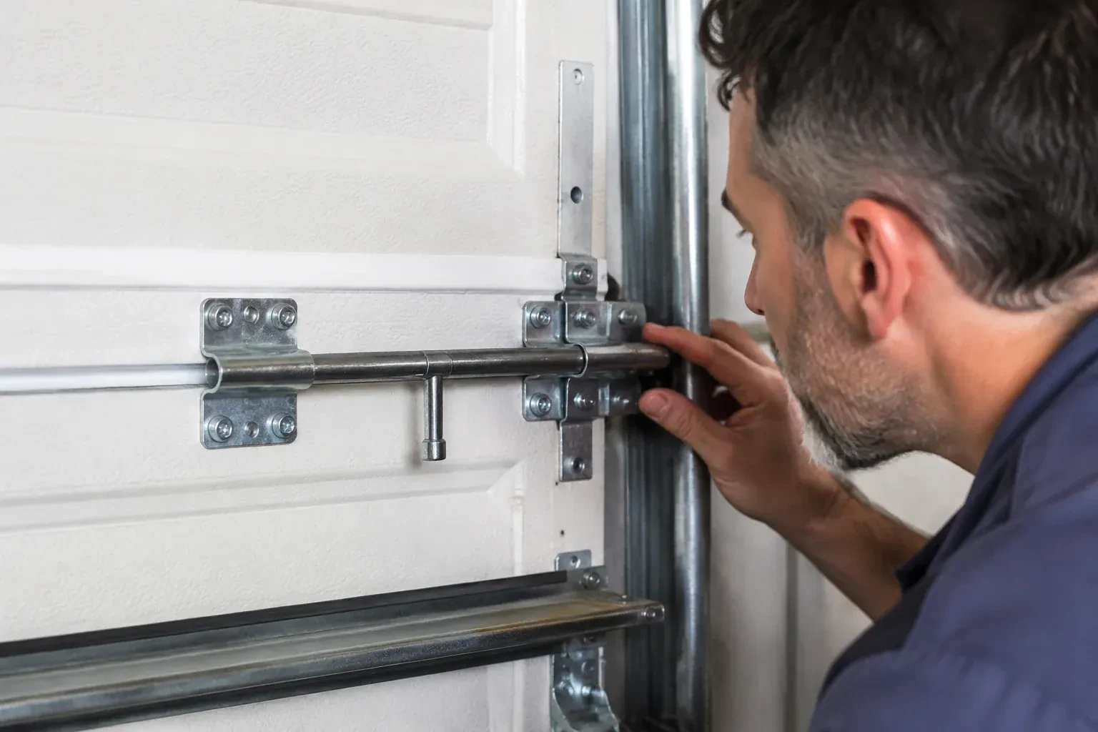 Person leaning close to a white paneled door, one hand on a metal slide-bolt bar mounted across the panel. — Garage Door Manual Lock Repair, Kawartha Lakes