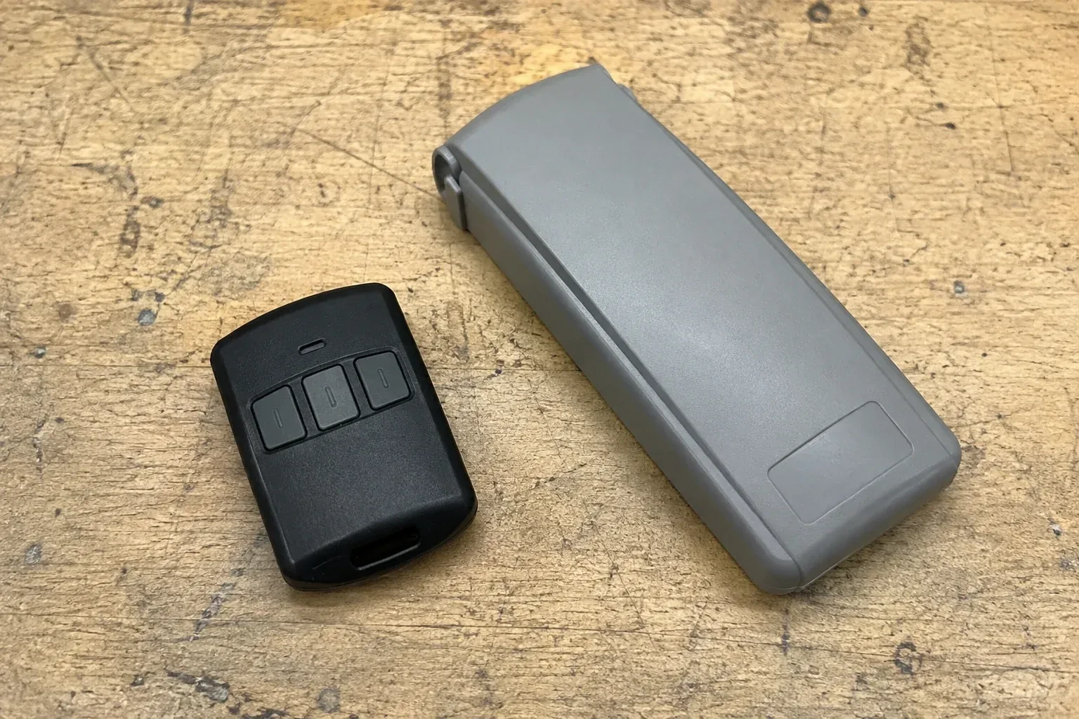 Three-button remote beside a closed grey keypad cover on a workbench. — Garage Door Remote and Keypad Programming, Kawartha Lakes
