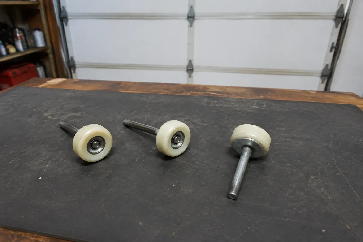 Three detached nylon-wheel garage door rollers with steel stems on a work mat. — Garage Door Roller Replacement, Kawartha Lakes